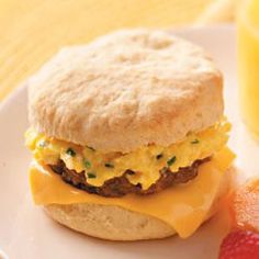 a breakfast sandwich with eggs and cheese on a plate next to oranges, strawberries and juice