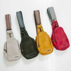 four different colored purses hanging on a white wall, one is black, the other is red