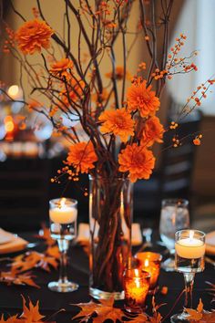 a vase filled with flowers and candles on top of a black tablecloth covered in leaves