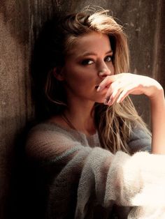 a woman leaning against a wall with her hand on her chin