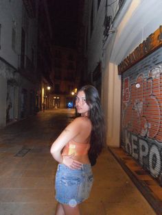 a woman standing in the middle of an alley way with her back turned to the camera