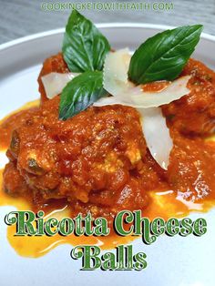 a white plate topped with meatballs covered in sauce and basil leaf garnish