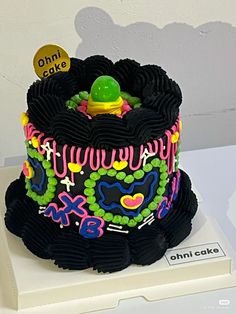 a black cake with neon colored icing and decorations on it's top is sitting on a white surface