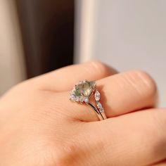 a woman's hand holding a ring with an oval shaped green diamond on it