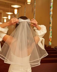 a woman in a white dress and veil covering her face with both hands while standing in front of a church pew