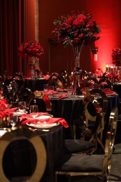 a room filled with tables covered in black and red cloths next to tall centerpieces