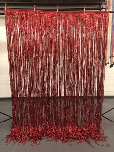 red tinsel hanging from the ceiling in front of a white wall and black floor