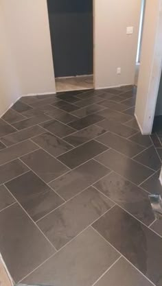 an empty room with tile flooring and door in the corner, looking into another room