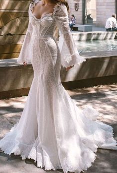 a woman in a white wedding dress standing on the sidewalk with her arms around her back