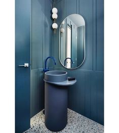 a bathroom with blue walls and a round mirror on the wall above it is a trash can