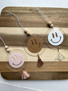 three wooden smiley faces with tassels hanging from them on a wood board,