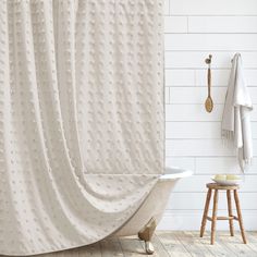 a bath tub sitting next to a wooden stool and shower curtain in a white bathroom