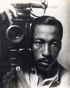 a black and white photo of a man holding an old camera in front of his face