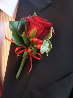 a boutonniere with red roses and green leaves on it's lapel