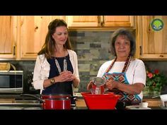 two women standing in a kitchen preparing food on top of a red pot and an electric blender