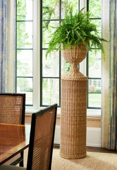 a large plant in a wicker basket on top of a wooden table next to a window