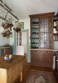 an old fashioned kitchen with wooden cabinets and pots hanging from the ceiling over the stove