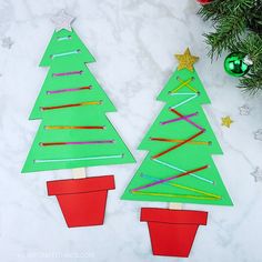 two christmas trees made out of construction paper on a white surface with ornaments around them