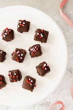 chocolate candies with sprinkles arranged on a white plate next to ribbon