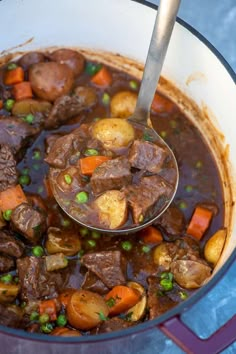 a ladle full of beef stew with potatoes and carrots is being spooned into the pot