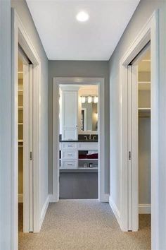 an empty hallway leading to a bathroom with white cabinets and drawers on either side of the door