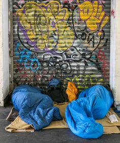 two sleeping bags are on the ground in front of a graffiti covered wall and door