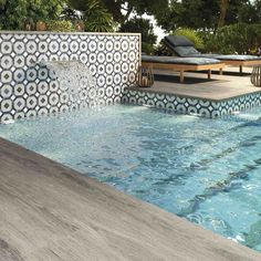 an outdoor swimming pool with water running from the side and lounges in the background