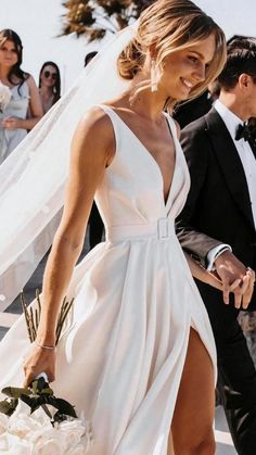 a woman in a white dress is walking down the street with a man in a tuxedo