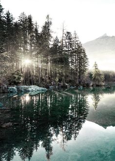 a lake surrounded by trees and mountains with the sun shining on it's surface