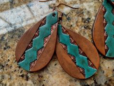 two brown and green leather earrings sitting on top of a marble counter