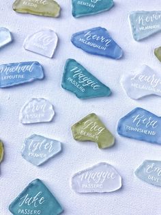 some blue and green sea glass with names on them sitting on a white tablecloth