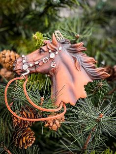 a horse head ornament hanging from a christmas tree with pine cones in the background