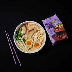 a bowl of ramen with chopsticks next to it on a black surface