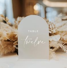 the table name is placed on top of some white flowers and feathers in front of it