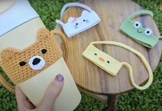 a person holding a coffee cup in front of three crocheted animal mug cozyies