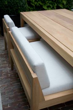 a wooden table with white cushions sitting on it's sides next to a brick walkway