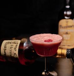 a pink drink in a glass next to liquor bottles