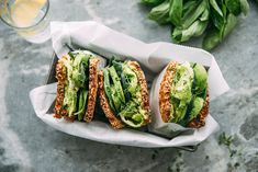 two sandwiches with lettuce and sesame seeds in wrappers next to a glass of orange juice