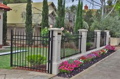 an iron fence with flowers growing on the top and bottom, in front of a house