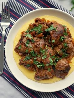 a white plate topped with meat and grits on top of a striped table cloth