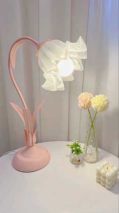 a pink lamp sitting on top of a table next to a vase filled with flowers