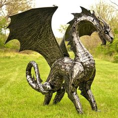 a metal dragon statue sitting on top of a lush green field