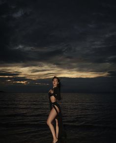 a woman standing on top of a beach next to the ocean at night with dark clouds