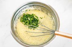 a metal bowl filled with cream sauce and chopped parsley in it on a white counter top