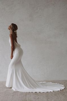 a woman in a white wedding dress is standing against a wall and looking off into the distance