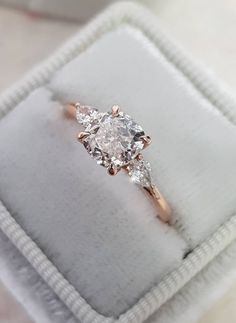 an engagement ring with three stones in it on a white cloth box that is sitting on top of a table