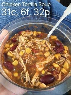 a person holding a bowl of chicken tortilla soup with beans and corn in it