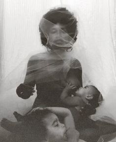 a woman sitting on top of a bed holding a baby next to another woman wearing a veil