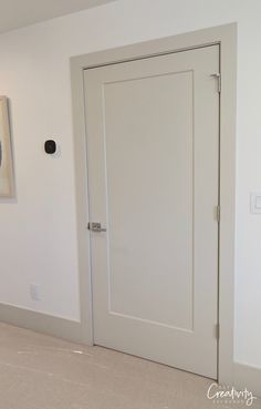 an empty room with two white doors and a painting on the wall behind it,