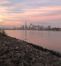 a view of the city skyline from across the water at sunset with rocks in foreground